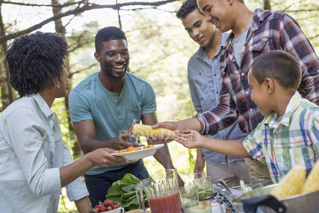 Adulti e bambini in piedi intorno a tavolo da picnic con cibo all'aperto . — Foto stock