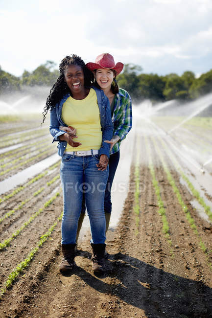 Две молодые женщины, стоящие в поле с поливочными дождевателями, распыляющими саженцы . — стоковое фото