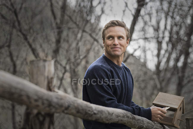Mittlerer erwachsener Mann in blauem Pullover posiert auf dem Land und lehnt am Zaun. — Stockfoto