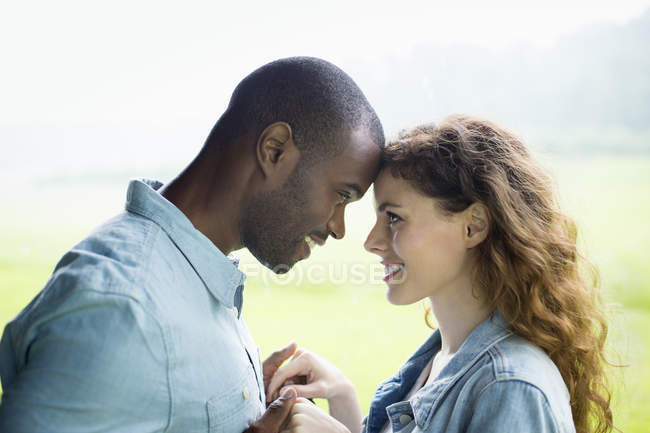 Young couple standing face to face and holding hands in green field and looking at each other. — Stock Photo