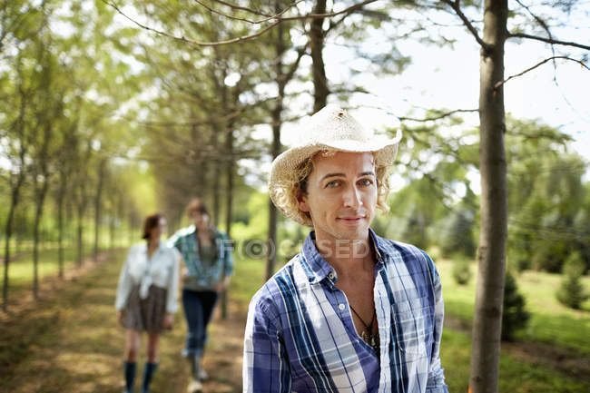 Молодой человек в шляпе ходит по тропинке летом с подружками на заднем плане
. — стоковое фото