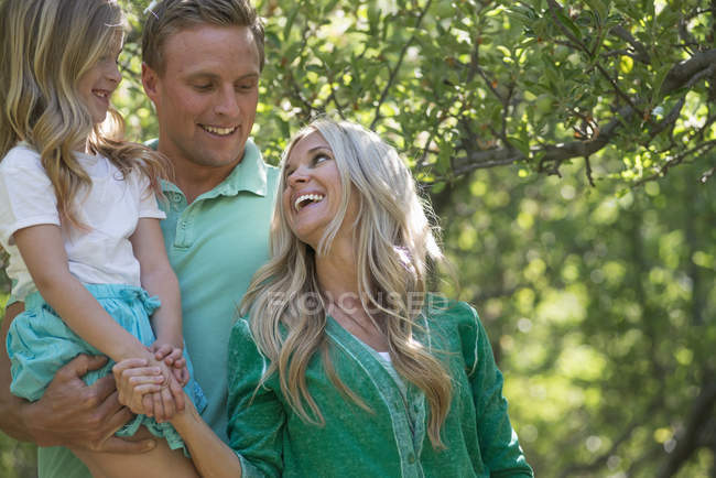 Parents with daughter standing in shade of trees in woodland. — Stock Photo