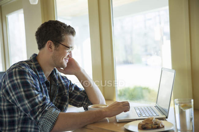 Young man sitting at cafe table and using laptop. — Stock Photo