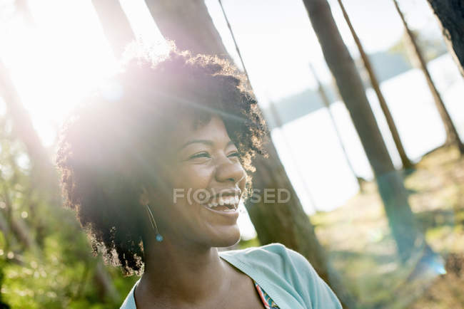 Young woman with curly black hair in shade of trees by lake shore in forest. — Stock Photo