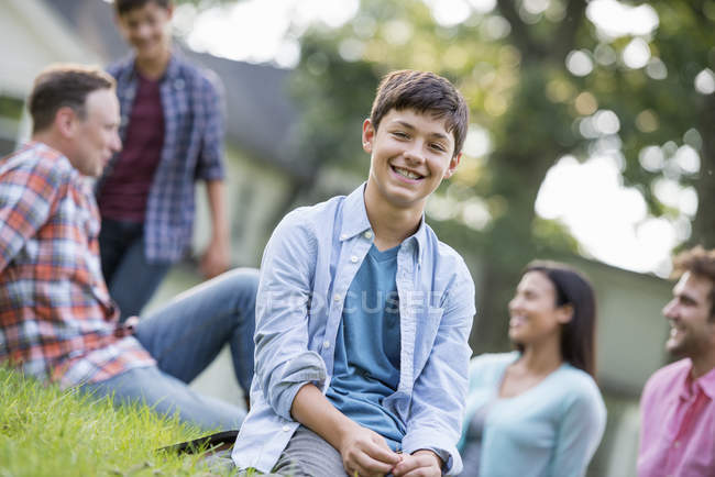 Menino pré-adolescente sentado na grama na festa de verão com a família . — Fotografia de Stock