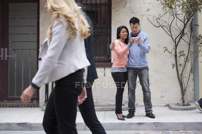 Pareja tomando selfie con smartphone con gente caminando por . - foto de stock