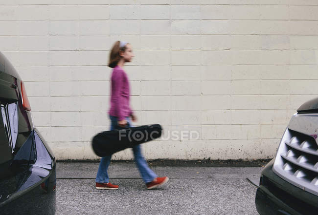 Vorpubertierendes Mädchen läuft mit Geigenkoffer auf Stadtstraße. — Stockfoto
