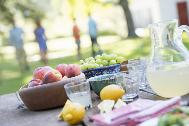 Served outdoor table with fruits and lemonade with people in background. — Stock Photo