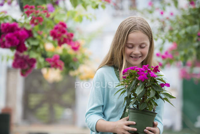 Pre-adolescent girl holding potted flowers at organic plant nursery and looking down. — Stock Photo