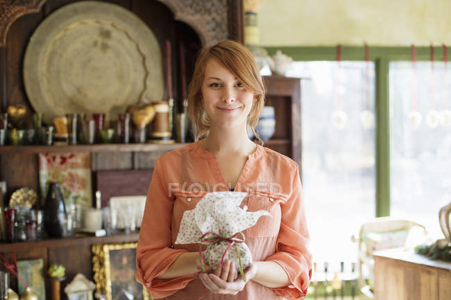 Young woman standing in antique store and holding tied packet with ribbon. — Stock Photo