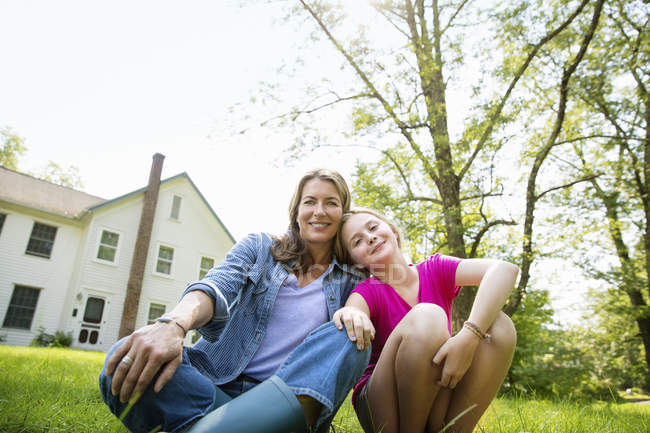 Mother with daughter sitting side by side in farmhouse green garden. — Stock Photo