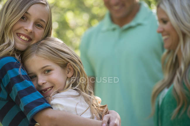 Parents avec des filles câlins debout à l'ombre des arbres dans les bois . — Photo de stock