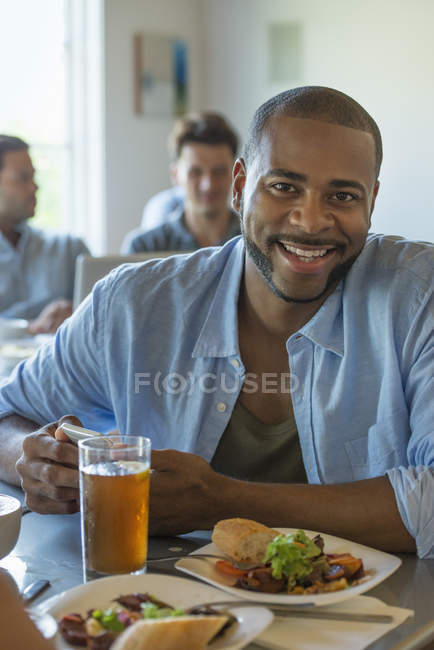 Homem sorrindo e olhando para a câmera na mesa de café com copo de cerveja . — Fotografia de Stock