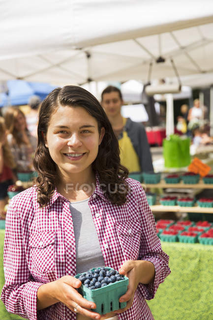 Junge Frau hält am Stand des Bauernmarktes eine Tüte Blaubeeren in der Hand. — Stockfoto