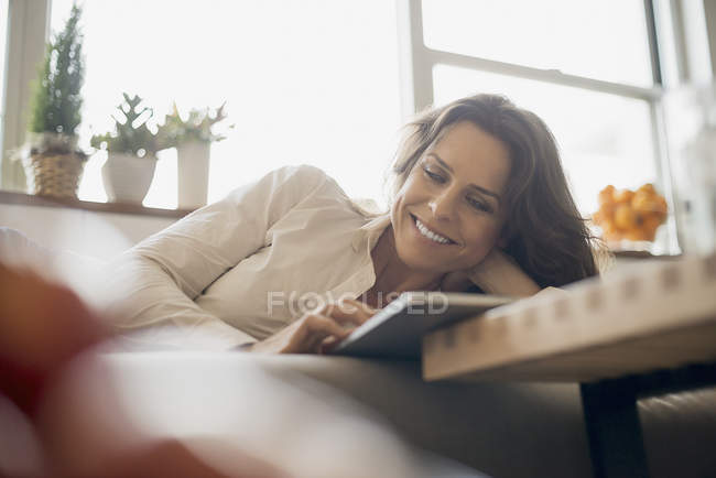 Женщина дома с цифровым планшетом на диване . — стоковое фото