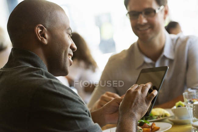 Hombre usando la mesa digital en la cafetería mientras almuerza con su colega
. - foto de stock