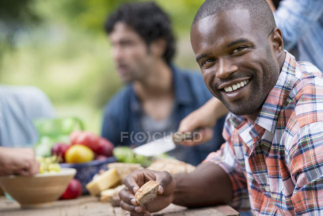 Средний взрослый мужчина держит хлеб и улыбается на открытом воздухе партии в саду . — стоковое фото