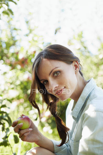 Jeune femme tenant une pomme fraîchement cueillie dans un arbre . — Photo de stock