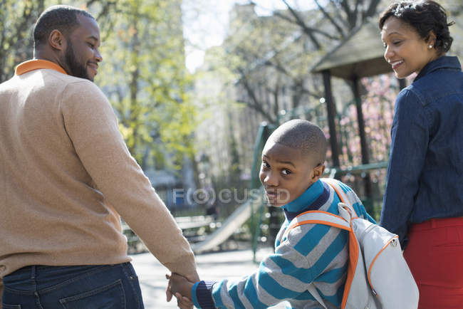 Ragazzo guardando oltre la spalla mentre cammina mano nella mano con i genitori sulla strada . — Foto stock