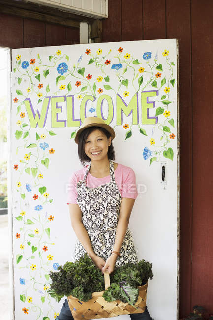 Молоді азіатські жінку, що стояли за Ласкаво просимо знак з кошиком свіжої зібрані зелений ферми овочі. — стокове фото