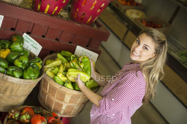 Mujer rubia joven clasificando pimientos para la venta en granja orgánica . - foto de stock