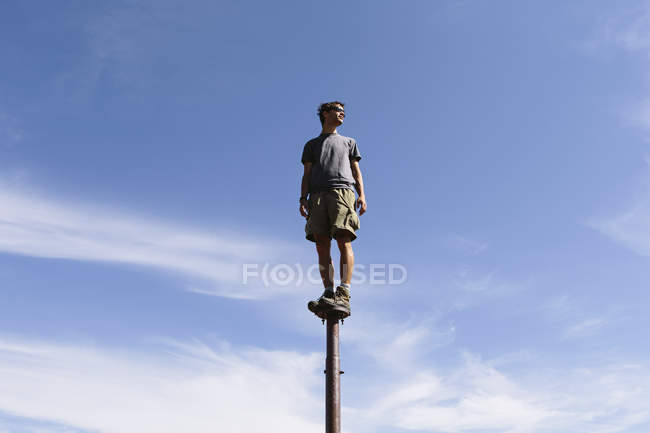 Людина балансує на металевому стовпі проти блакитного неба з хмарами . — стокове фото
