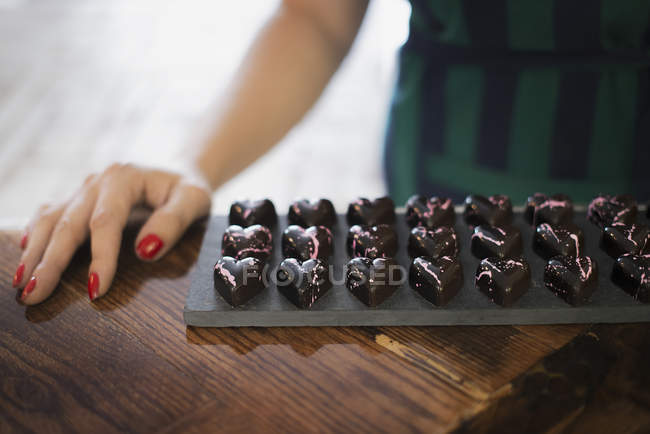 Крупним планом жіноча рука і лоток формованих шоколадних цукерок . — стокове фото