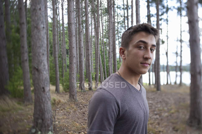 Молодий чоловік дивиться в камеру, стоячи в лісі . — стокове фото