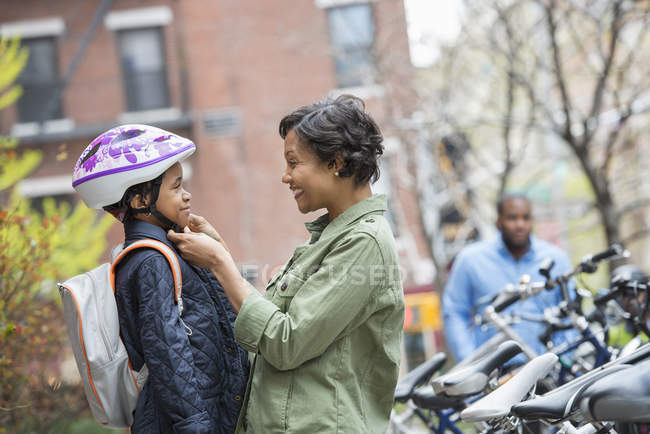 Mother fastening cycle helmet on son beside bicycle rack with man in background. — Stock Photo