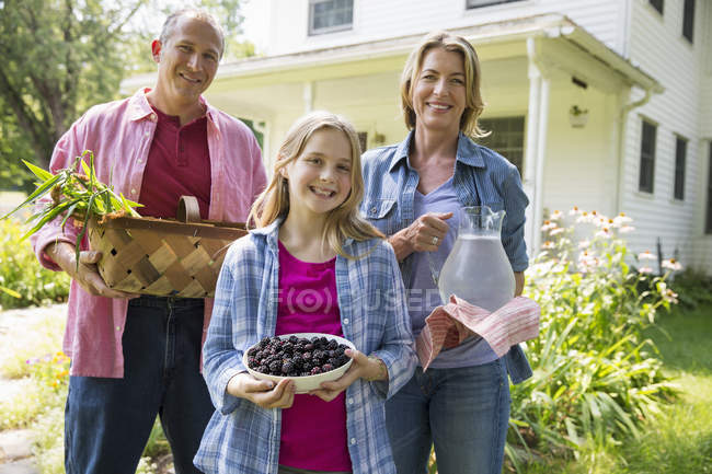 Familie posiert mit Brombeeren, Gemüse und einem Krug Limonade im Bauerngarten. — Stockfoto