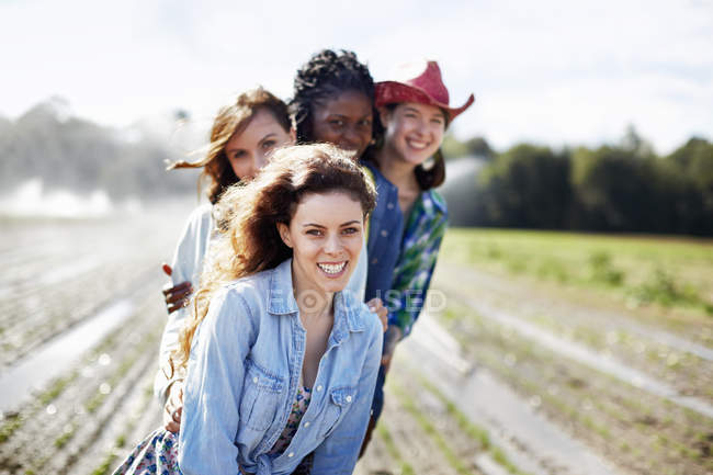 Young female friends in field with sprinklers spraying water at seedlings. — Stock Photo