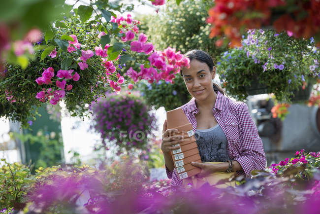 Mujer joven llevando pila de macetas en vivero de plantas de flores . - foto de stock