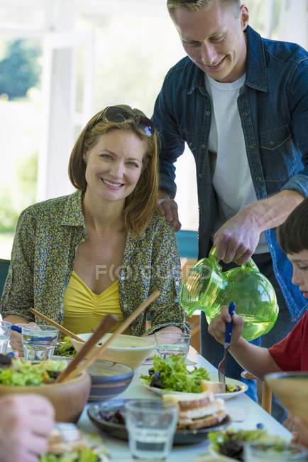Uomo versando bevanda dalla brocca con la famiglia a tavola . — Foto stock