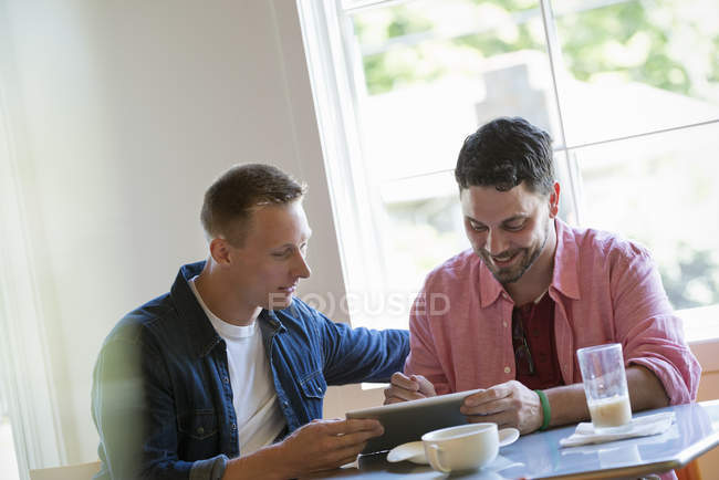 Deux hommes utilisant la tablette numérique ensemble à la table de café . — Photo de stock