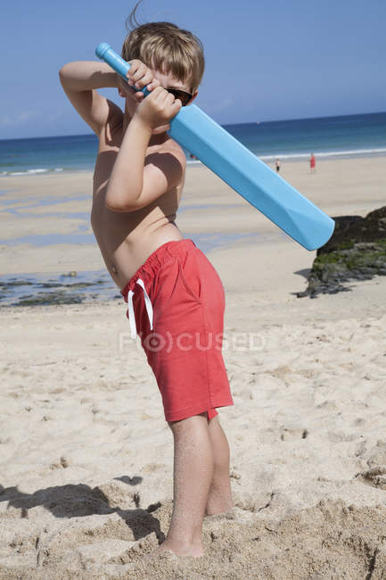 Хлопчик стоїть на піску з маленькою синьою крикетною кажаною в руках . — стокове фото