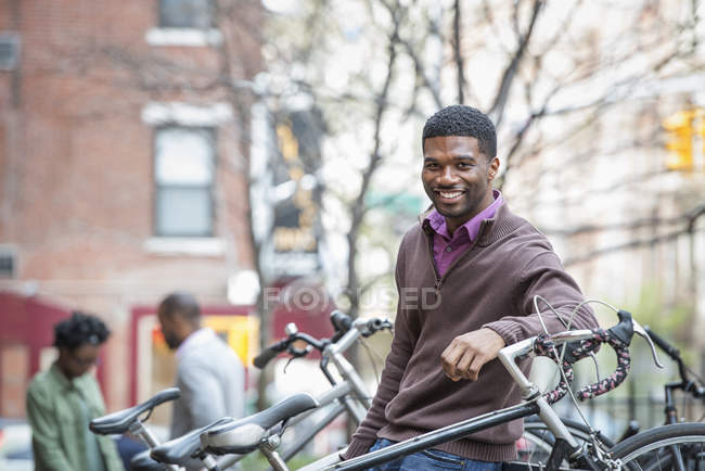 Jovem se apoiando no rack de bicicleta e sorrindo na câmera . — Fotografia de Stock