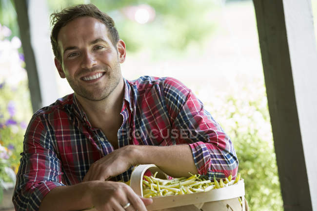 Young man holding basket of beans at farmer market stand. — Stock Photo