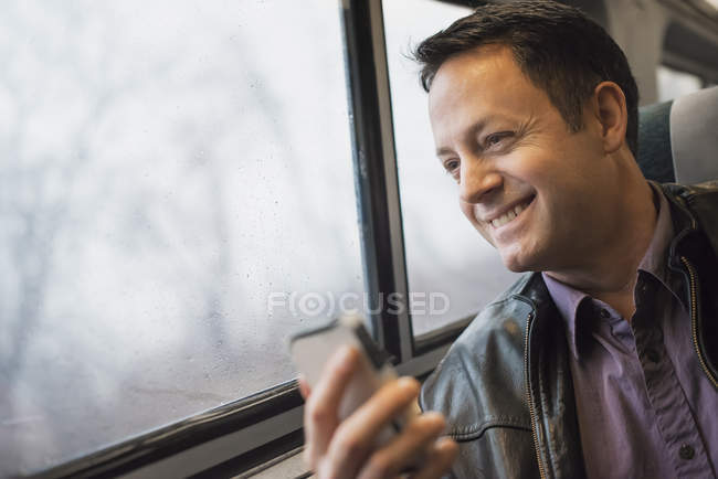Älterer Mann sitzt am Fensterplatz im Zug und hält Handy in der Hand. — Stockfoto
