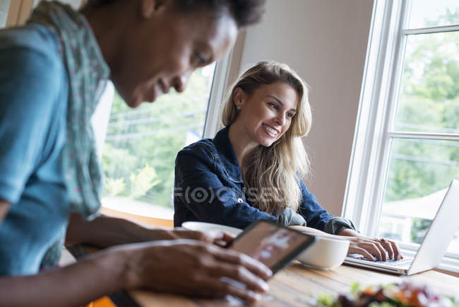 Two women in cafe using digital tablet and laptop while lunch. — Stock Photo