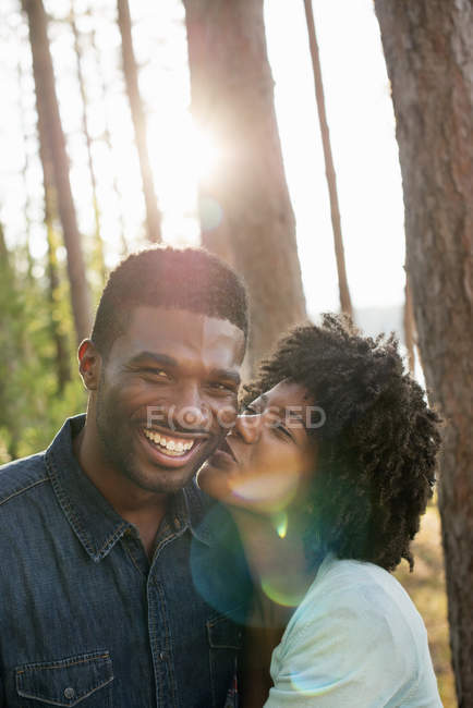 Young woman kissing man on cheek in sunny woods. — Stock Photo