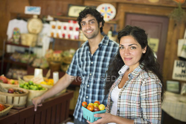 Jeune homme et femme avec récipient de tomates mûres au magasin de producteurs biologiques . — Photo de stock