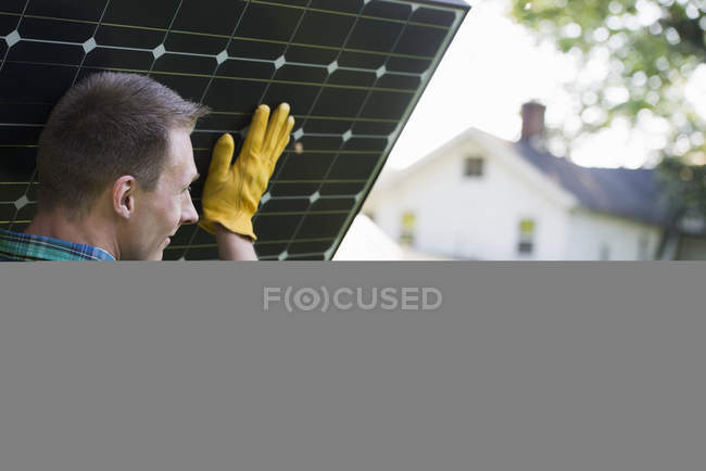 Man carrying solar panel towards building in countryside. — Stock Photo