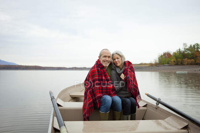 Maturo uomo e donna seduti in barca a remi avvolti in una calda coperta
. — Foto stock