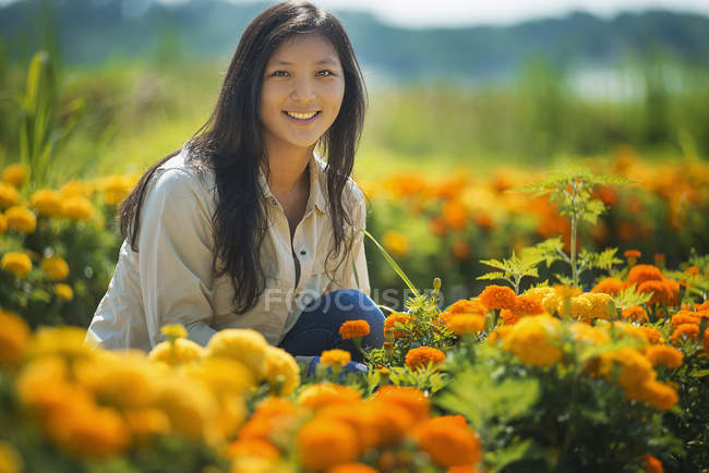 Mujer joven agachada en el jardín rodeada de flores de color naranja . - foto de stock