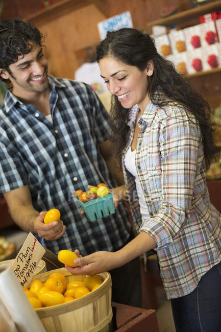 Un jeune homme et une jeune femme trient les tomates dans un magasin d'agriculteurs biologiques . — Photo de stock