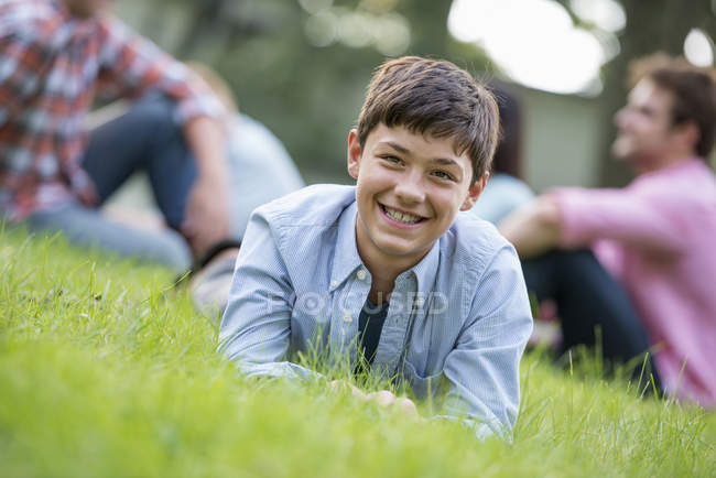 Pre-adolescente niño acostado en la hierba en la fiesta de verano con la familia . - foto de stock