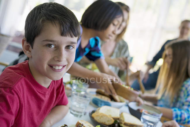 Pre-adolescente niño sonriendo y mirando en cámara con los niños en la mesa de la cena . - foto de stock