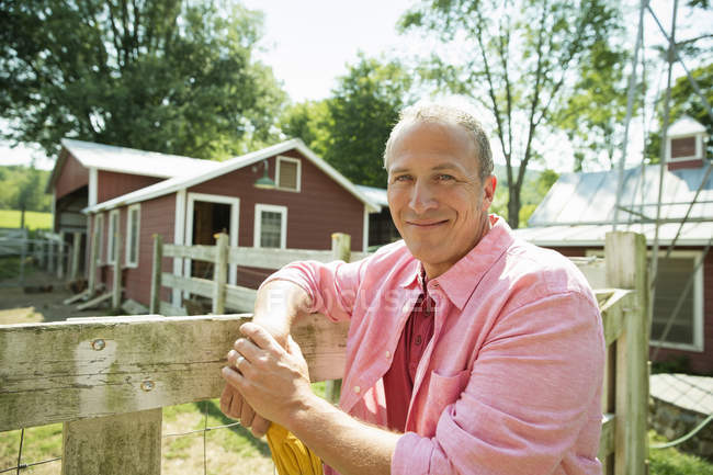 Mature man leaning on wooden fence at farmhouse garden. — Stock Photo