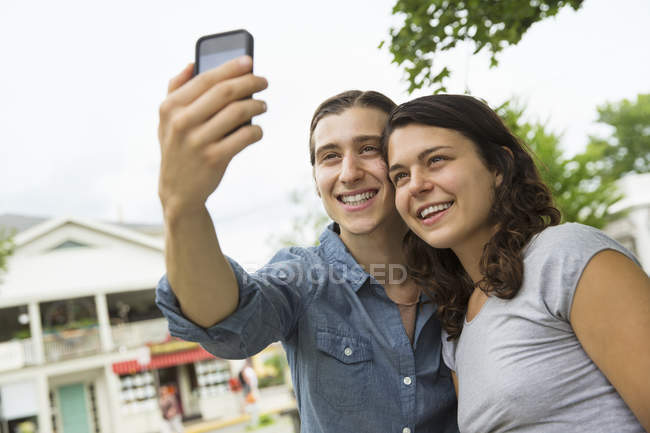 Jovem casal de pé lado a lado e tomando selfie na rua . — Fotografia de Stock