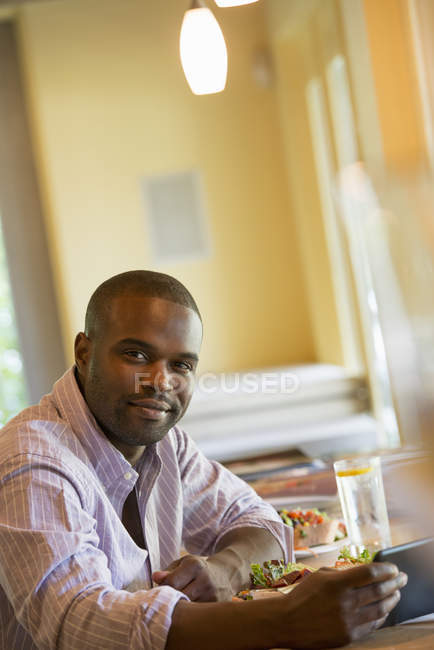 Jeune homme assis à table dans un café et utilisant une tablette numérique . — Photo de stock